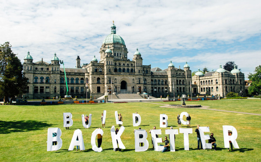 Dogwood volunteers holding five foot letters that spell out 'Build BC Back Better' on the Legislature lawn with the Legislature building in the background.