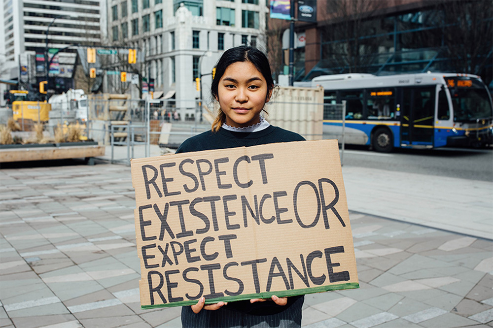 Young activist stands with a sign that says Respect existence or expect resistance. Let youth lead.