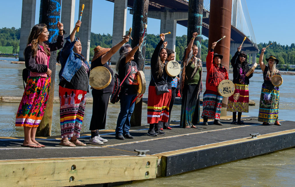 Indigenous leaders drumming on a dock on the Fraser river