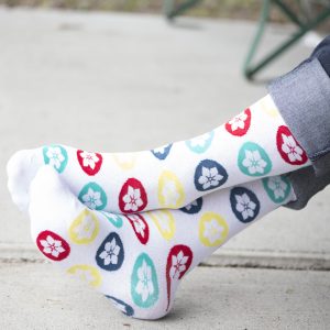 Up close shot of crossed feet wearing white socks with multi-coloured Dogwood logo flower icon pattern.