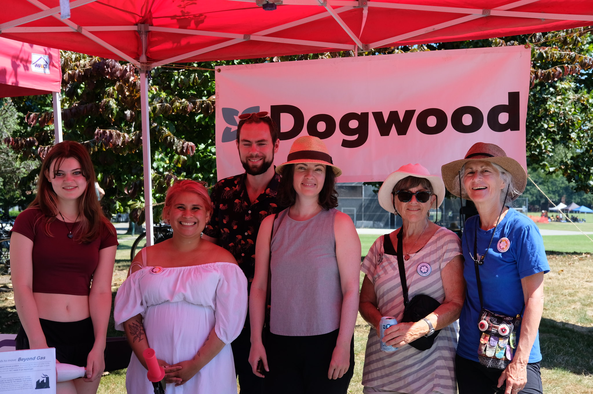 Group of six people smiling for the camera in front of hung banner that reads 'Dogwood' under a pop up tent with trees in the background.